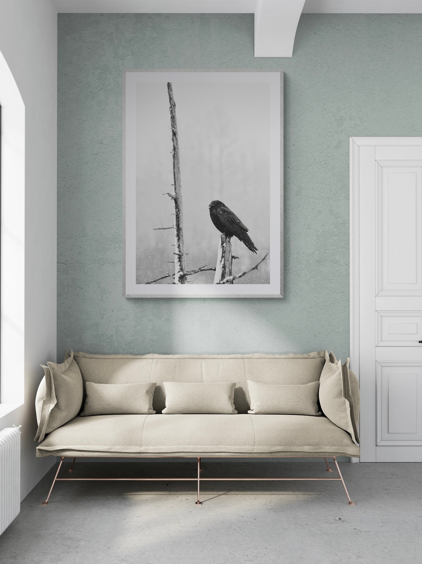 Black and white photograph of a bird perched on a branch in a modern living room setting with neutral decor.