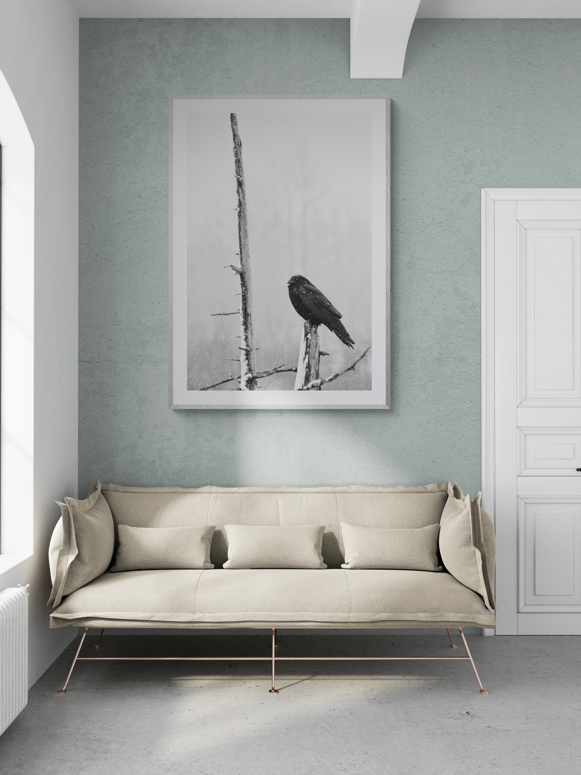Black and white photograph of a bird perched on a branch in a modern living room setting with neutral decor.